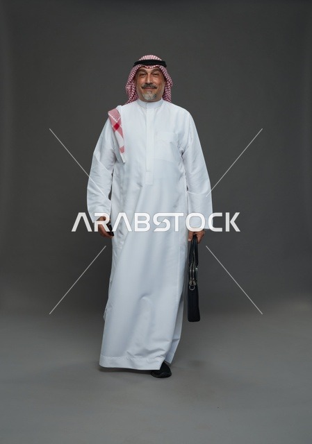 رجل أعمال سعودي مسن يحمل حقيبة عمل وهاتف ذكي