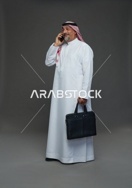 رجل أعمال سعودي يتحدث بالهاتف مع حقيبة عمل