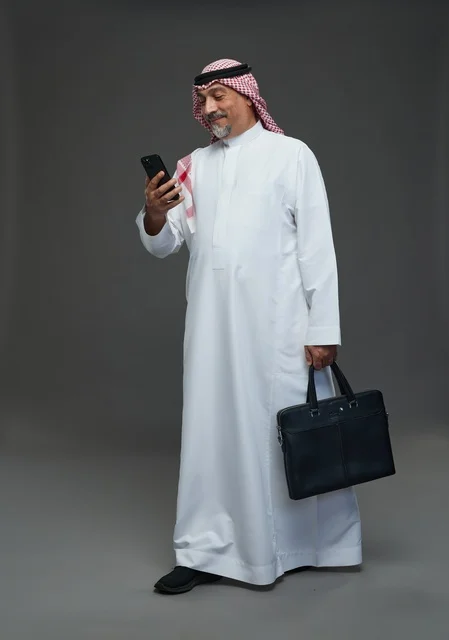 رجل أعمال سعودي مسن يتفقد هاتفه المحمول ويحمل حقيبة عمل