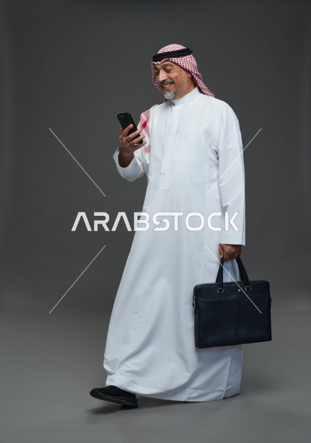 رجل أعمال سعودي مسن يحمل هاتفه وحقيبة عمل