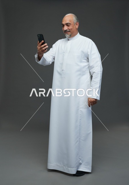 Elderly Saudi Man Using Smartphone on Grey Background