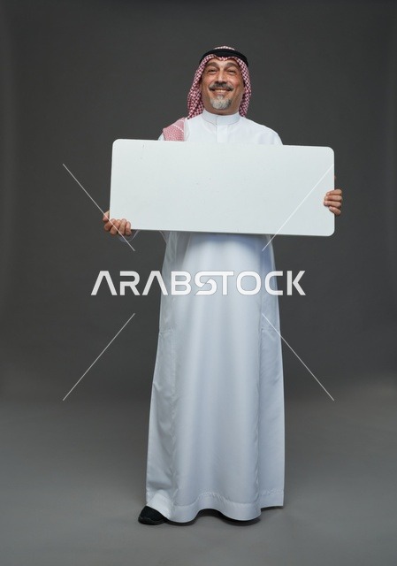 رجل سعودي مسن يرتدي الزي التقليدي يحمل لوحة إعلانية فارغة