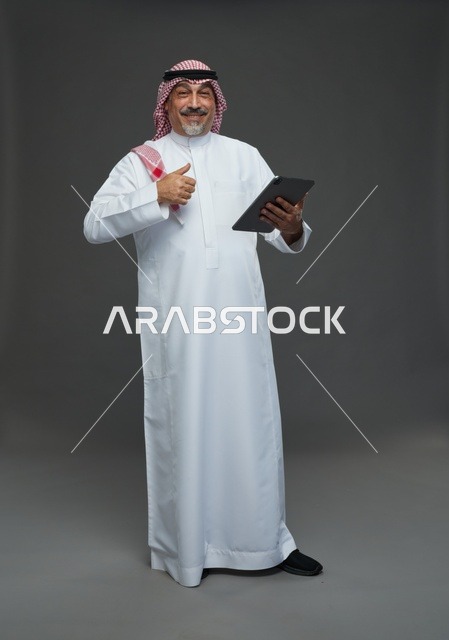 رجل سعودي مسن يستخدم جهاز لوحي في استوديو بخلفية رمادية