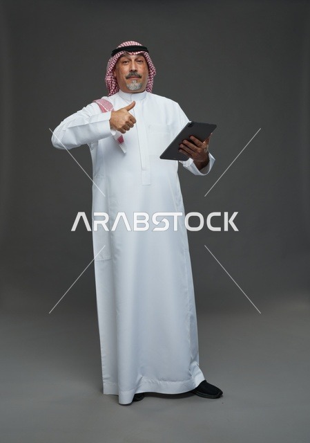رجل سعودي مسن يستخدم جهاز لوحي وإيماءة الإبهام