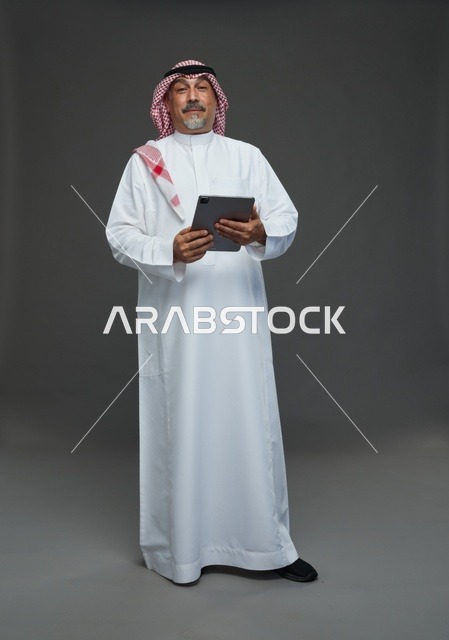 رجل سعودي مسن يحمل جهاز لوحي في الاستوديو