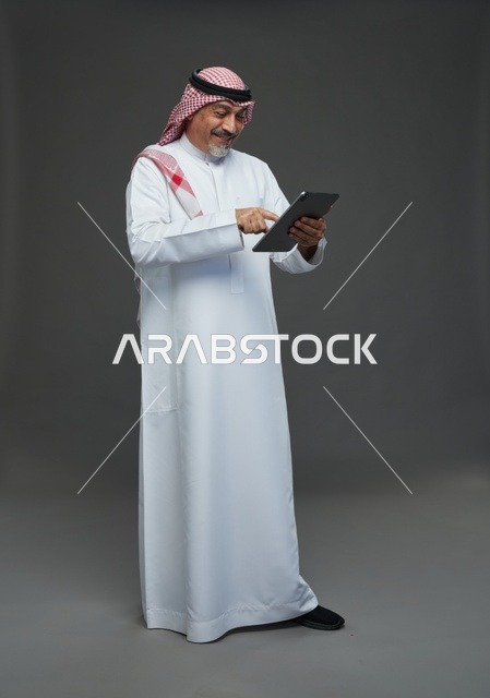 Senior Saudi Man Using Tablet on Grey Background
