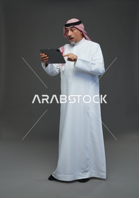 Elderly Saudi Man Using Tablet on Gray Background