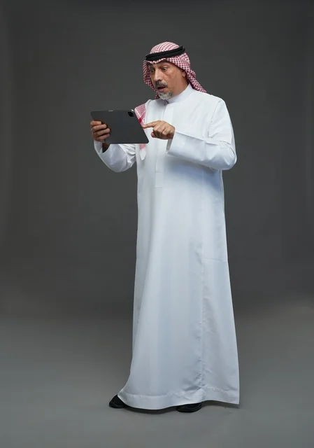 Elderly Saudi Man Using Tablet on Gray Background