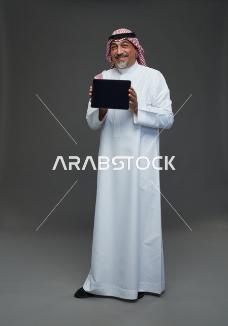 رجل سعودي مسن يحمل جهاز لوحي في الاستوديو
