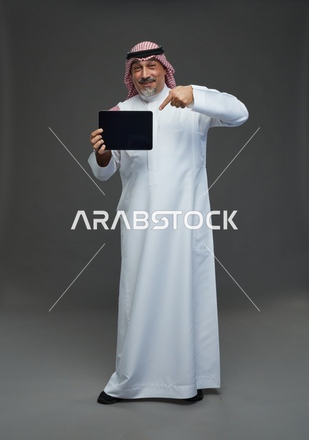 رجل سعودي مسن يشير إلى جهاز لوحي في الاستوديو