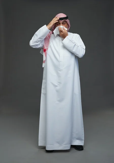 رجل سعودي مسن يعطس في منديل بخلفية رمادية