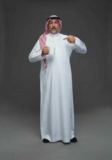 رجل سعودي مسن يحمل كوب قهوة أبيض في الاستوديو