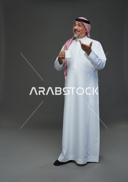رجل سعودي مسن يحمل كوب قهوة أبيض في استوديو