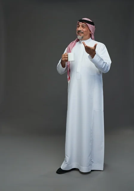 رجل سعودي مسن يحمل كوب قهوة أبيض في استوديو