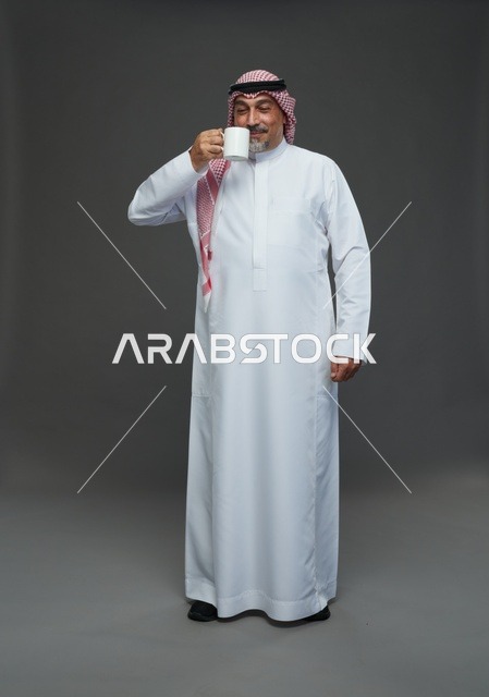رجل سعودي مسن يمسك كوب قهوة أبيض في استوديو