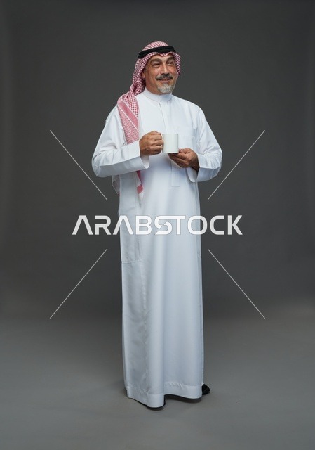 رجل سعودي مسن يحمل كوب قهوة أبيض في الاستوديو