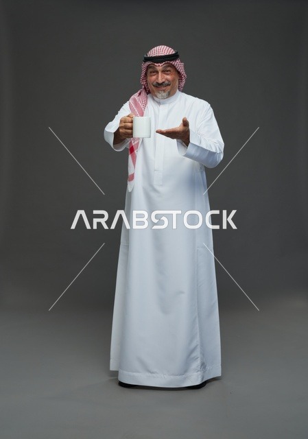 رجل سعودي مسن يحمل كوب قهوة أبيض في استوديو