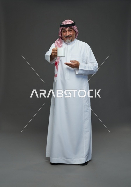 رجل سعودي مسن يحمل كوباً أبيض في استوديو