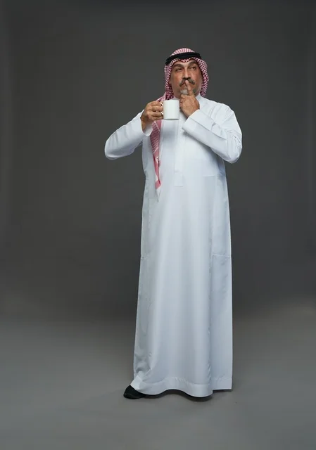 رجل سعودي بالزي التقليدي يحمل كوب قهوة أبيض