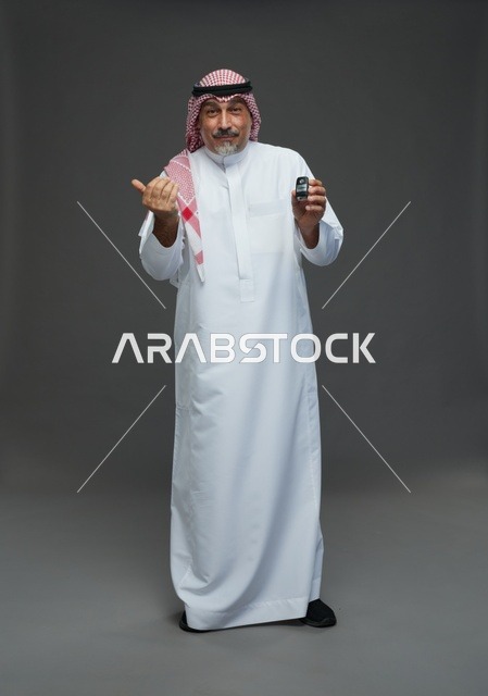 رجل سعودي يحمل مفتاح سيارة بخلفية رمادية