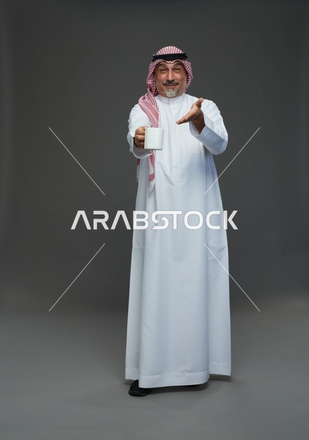 رجل سعودي مسن يحمل كوب قهوة أبيض في استوديو