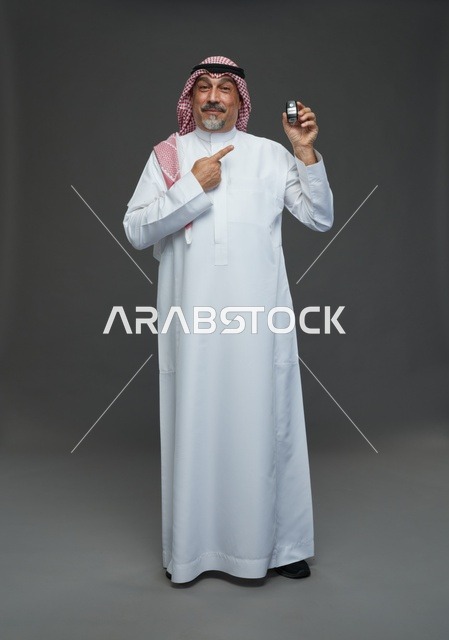 رجل سعودي يحمل مفتاح سيارة بابتسامة في استوديو تصوير