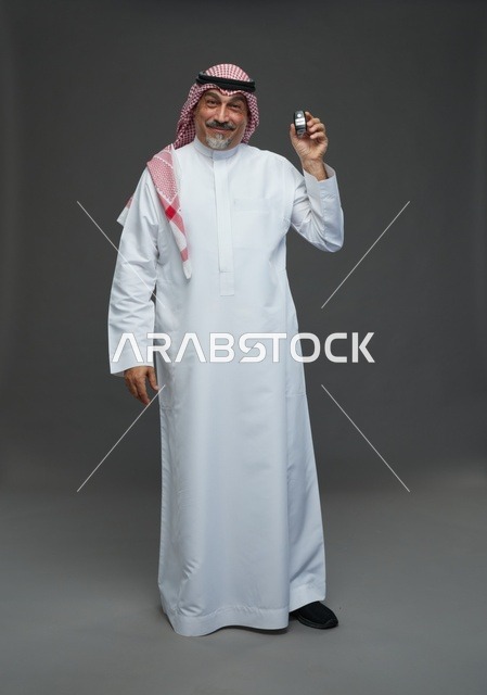 رجل سعودي يحمل مفتاح سيارة بخلفية رمادية