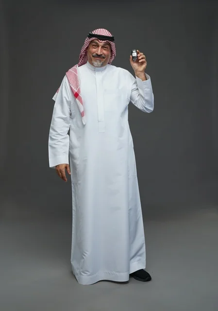 رجل سعودي يحمل مفتاح سيارة بخلفية رمادية