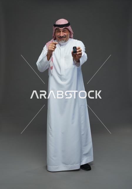 رجل سعودي يحمل مفتاح سيارة بخلفية رمادية