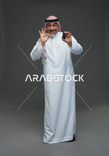 رجل سعودي يحمل مفتاح سيارة بوضعية موافق في الاستوديو