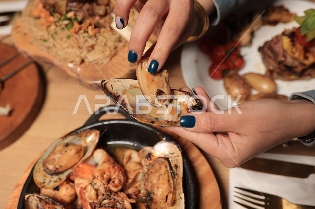 يد سيدة تتناول محار البحر اللذيذ ، بلح البحر ، حيوانات صدفية مائية ،ماكولات بحرية ، مطاعم عربية 