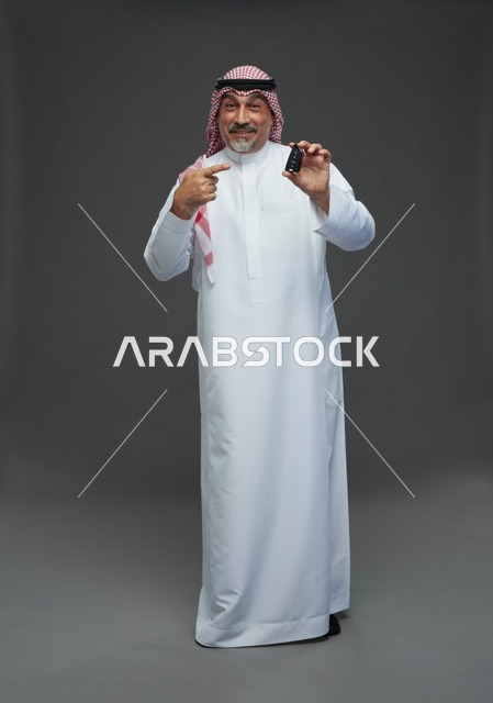 رجل سعودي في استوديو يمسك مفتاح سيارة بخلفية رمادية