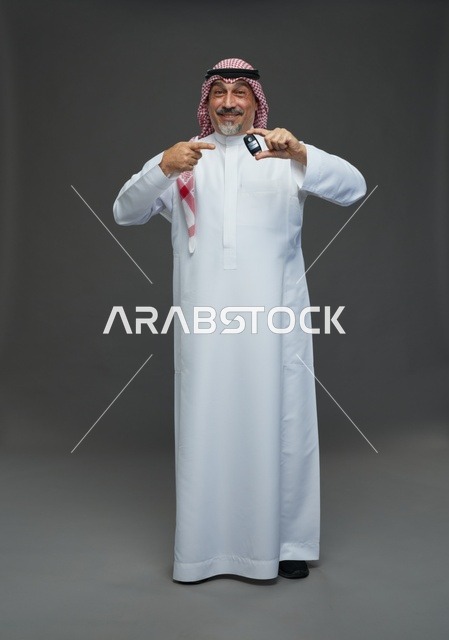 رجل سعودي يحمل مفتاح سيارة على خلفية رمادية