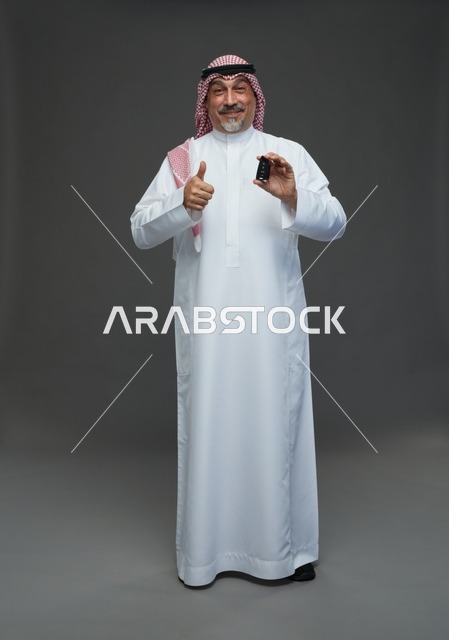 رجل سعودي يحمل مفتاح سيارة ويشير بعلامة الإعجاب