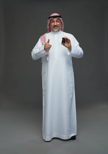 رجل سعودي يحمل مفتاح سيارة ويشير بعلامة الإعجاب