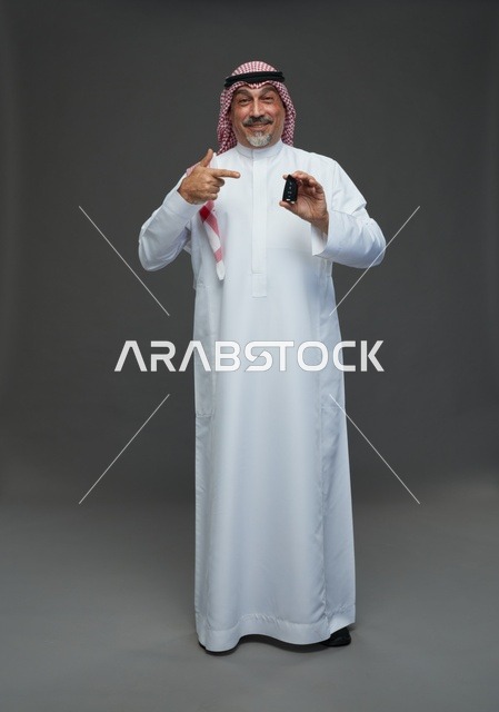 رجل سعودي يحمل مفتاح سيارة أمام خلفية رمادية