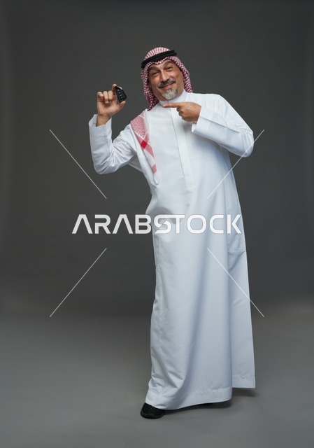 رجل سعودي يحمل مفتاح سيارة بخلفية رمادية