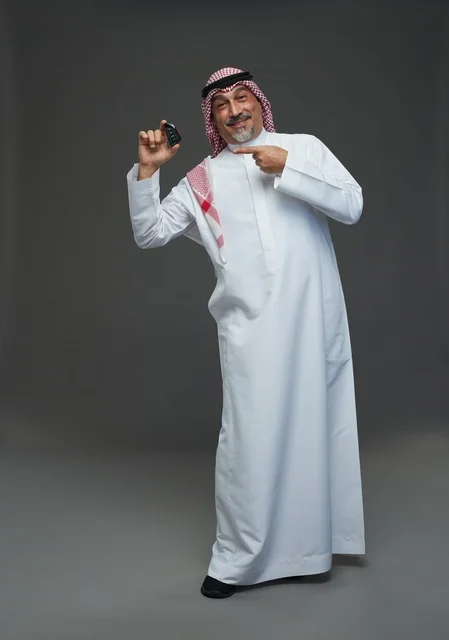 رجل سعودي يحمل مفتاح سيارة بخلفية رمادية