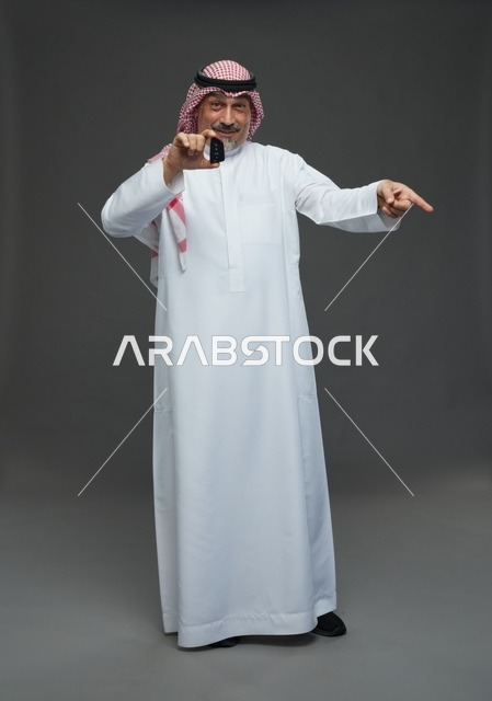 رجل سعودي يحمل مفتاح سيارة بخلفية رمادية