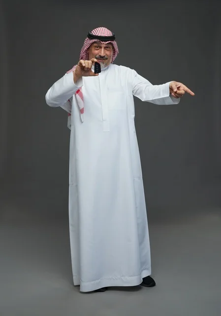 رجل سعودي يحمل مفتاح سيارة بخلفية رمادية