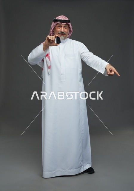 رجل سعودي يحمل مفتاح سيارة ويشير أمام خلفية رمادية