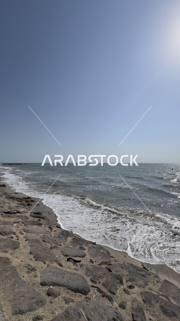 ساحل صخري وأمواج البحر تحت سماء زرقاء صافية مشمسة