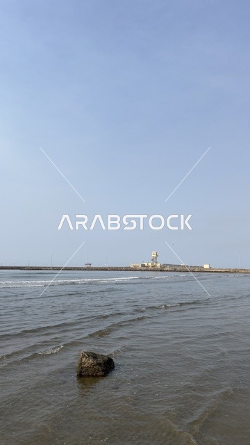 شاطئ بحري ساحلي مع أمواج وصخرة ورصيف بعيد