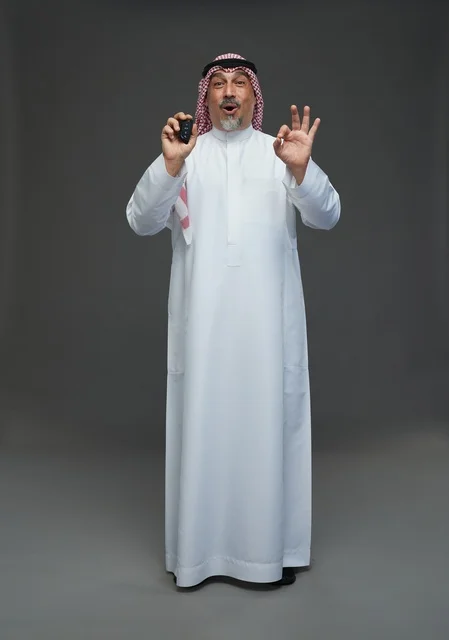 رجل سعودي بزي تقليدي يحمل مفتاح سيارة مع تعابير دهشة