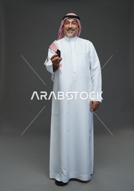 رجل سعودي بالثوب يحمل مفتاح سيارة أمام خلفية رمادية