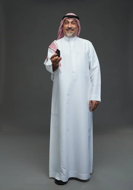 Saudi Man in Thobe Holding Car Key on Grey Background
