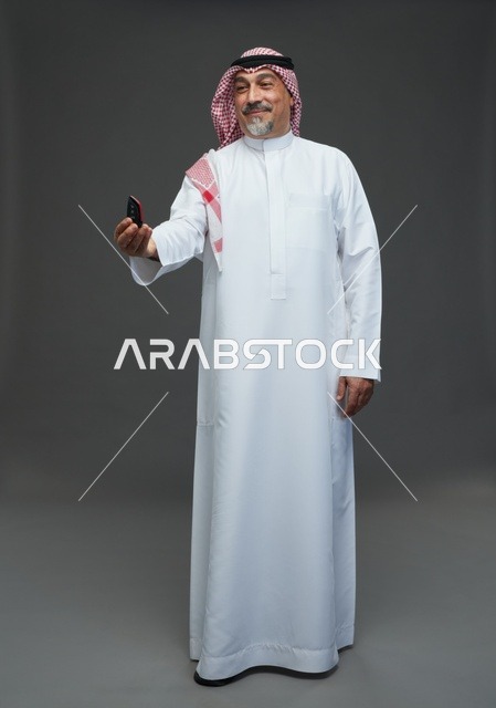 رجل سعودي بالزي التقليدي يمسك مفتاح سيارة في الاستوديو