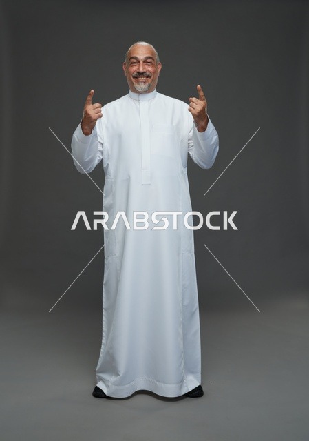 رجل سعودي يرتدي الثوب التقليدي ويشير للأعلى بابتسامة عريضة