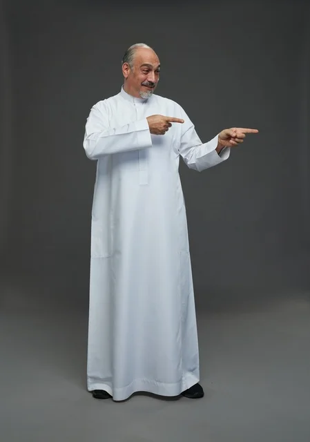 رجل عربي سعودي مسن يرتدي الثوب التقليدي ويشير إلى الجانب