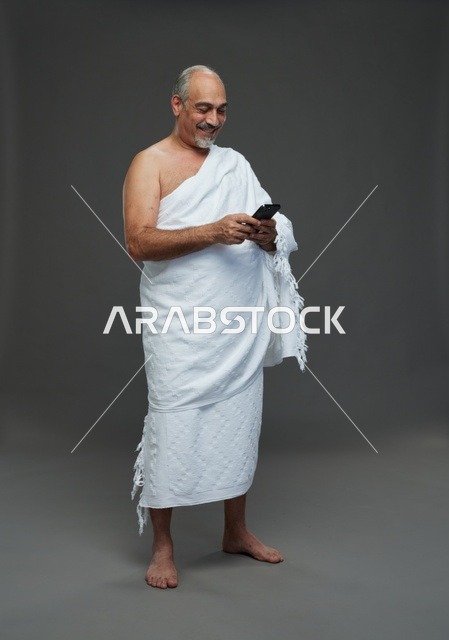 رجل عربي بملابس الإحرام يستخدم الهاتف الذكي في استوديو